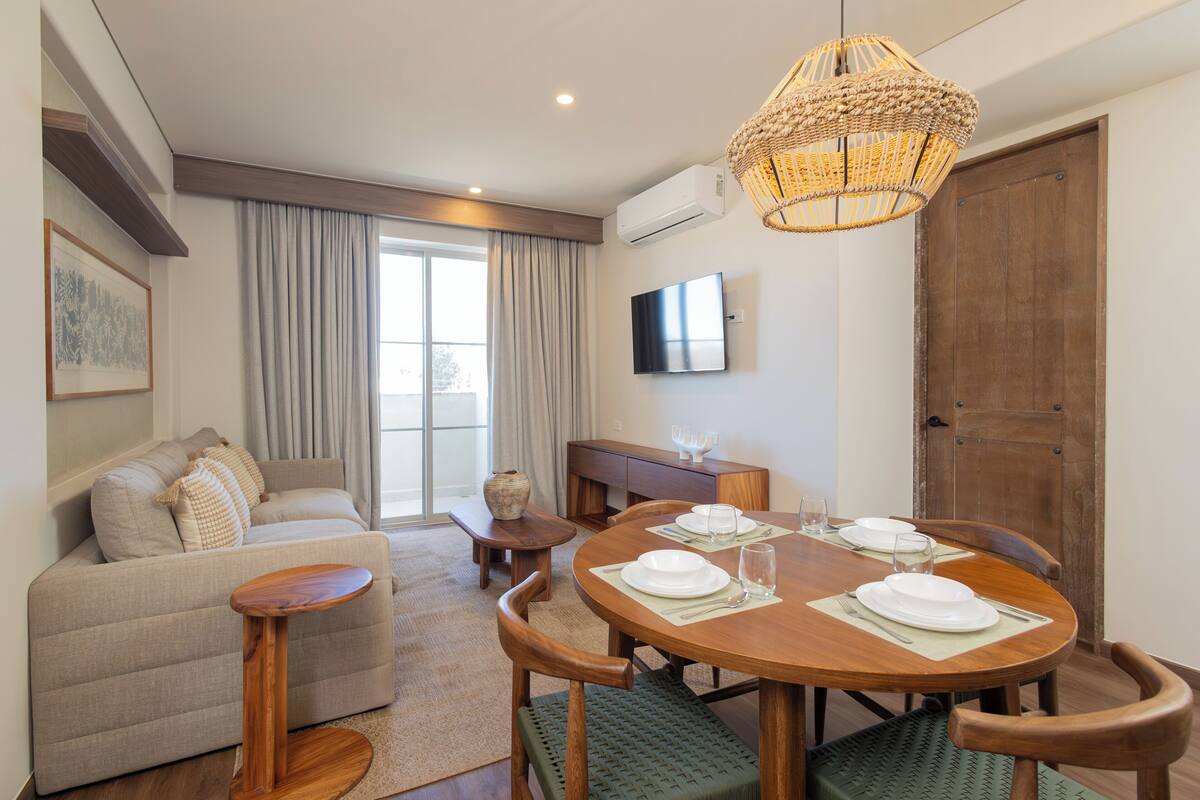 A modern living room with a sofa, dining table set for four, and a television mounted on the wall.