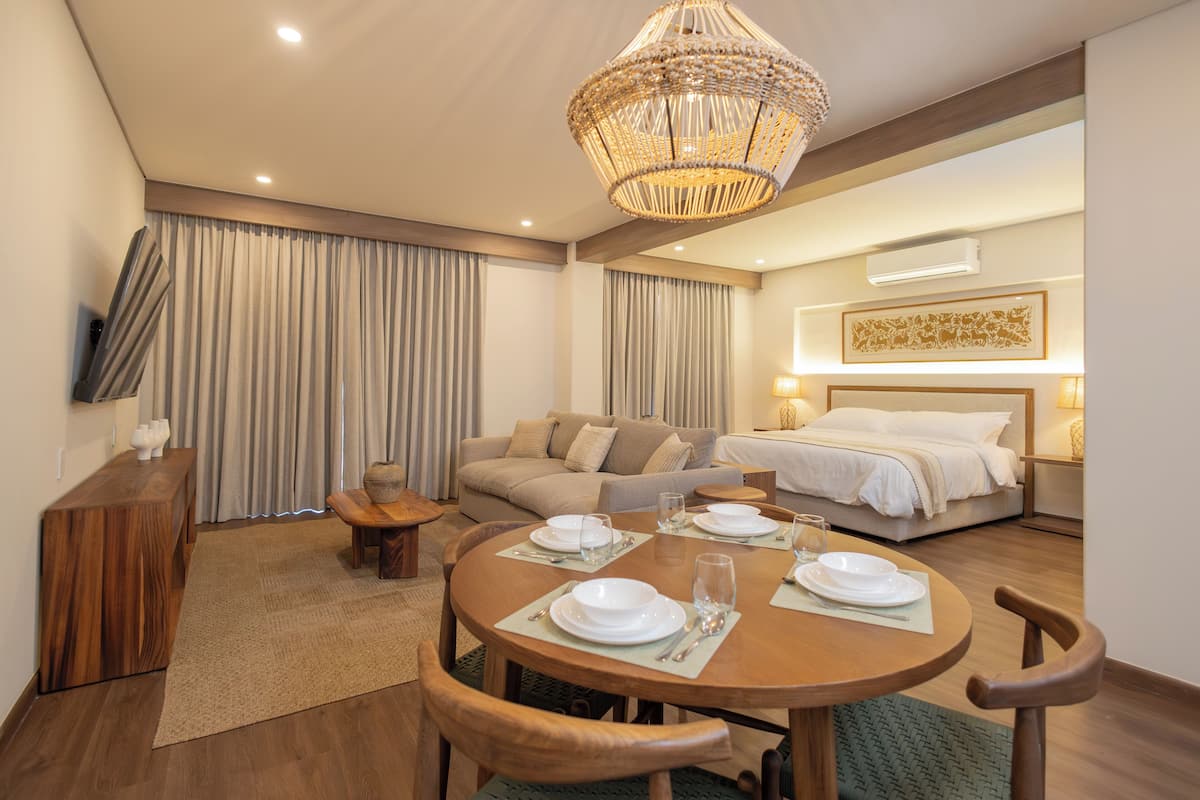 A hotel room with a dining area, a sofa, a bed, and a television on the wall.
