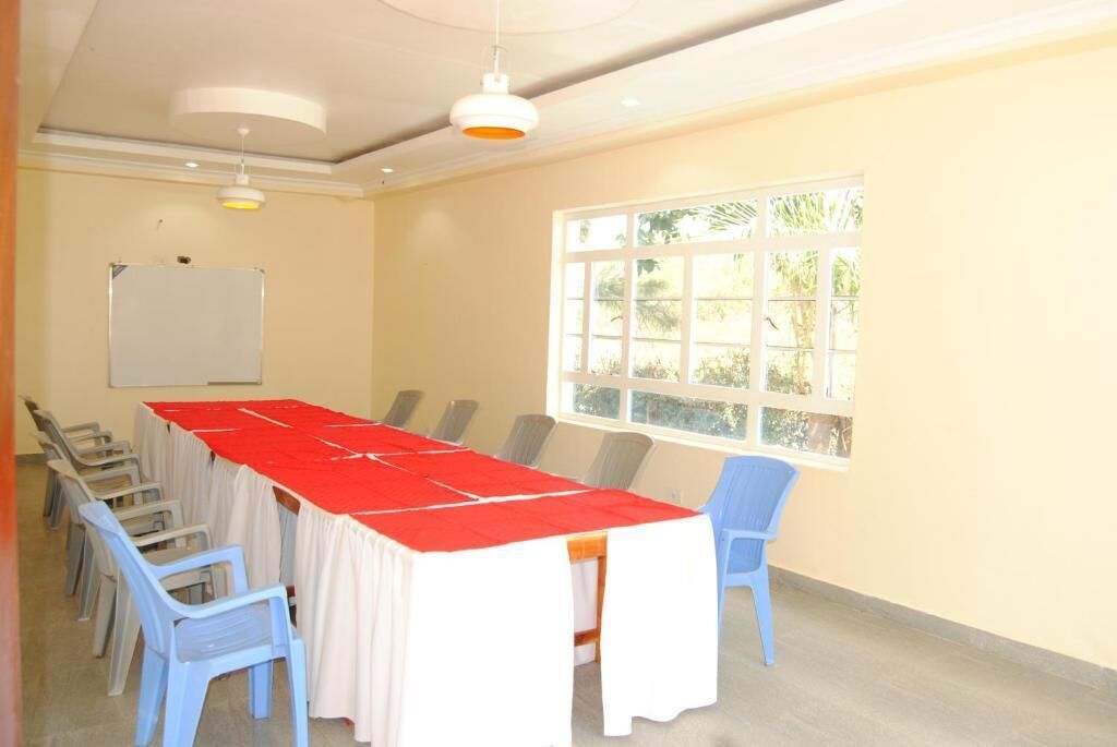 A conference room with a long table, white chairs, and a red tablecloth. There is a whiteboard on the wall and a window with a view of greenery.