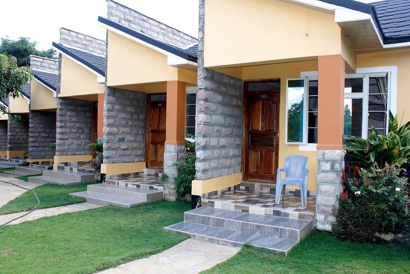 A row of modern houses with stone pillars, wooden doors, and a paved driveway.