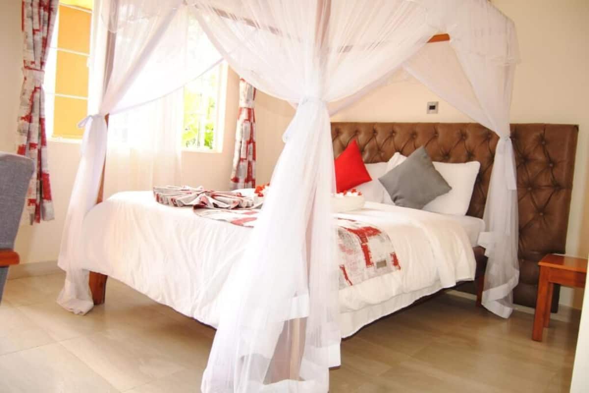 A bedroom with a four-poster bed, a tufted headboard, and a window with curtains.