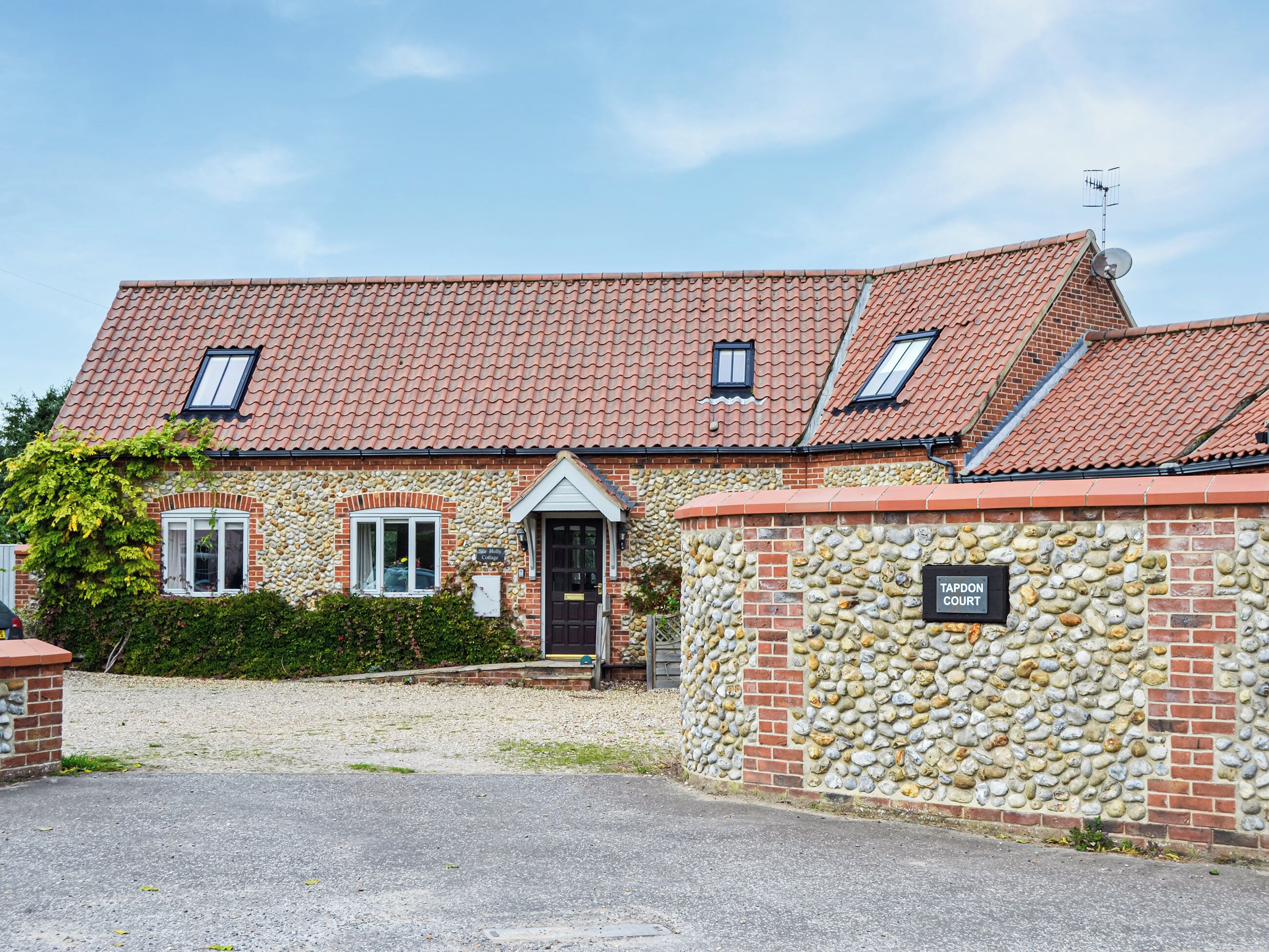 A stone building with a tiled roof, a stone wall with a sign, and a gravel driveway.