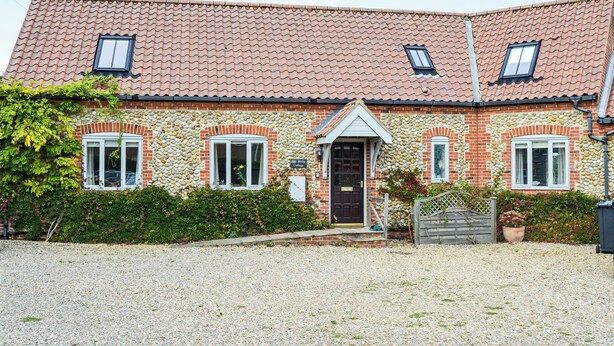 Ein zweigeschossiges Haus mit Ziegeldach, Backsteinfassade und Auffahrt mit Kies.