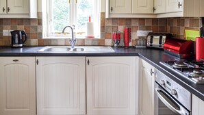 Eine Küche mit weißen Schränken, einer Edelstahlspüle, einem Fenster mit Blumenmuster-Vorhang und einem roten Toaster.