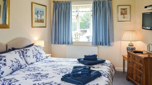 Ein Schlafzimmer mit Bett, Kommode, Lampe und einem Fenster mit Vorhängen.