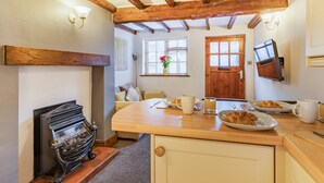 Eine gemütliche Küche mit Holzbalken, Kamin, einer Frühstückstherme und einem an der Wand befestigten Fernseher.