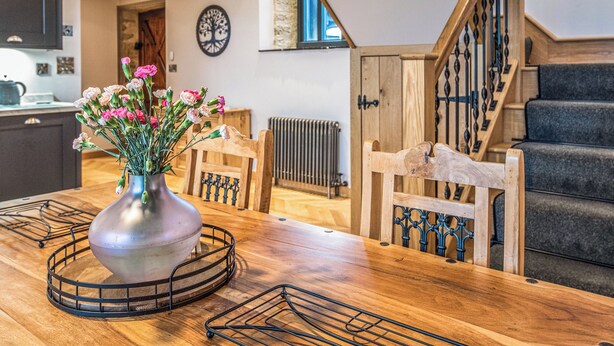 Ein Holzespeisetisch mit einer Metallvase voller Blumen, eine Küche im Hintergrund und eine Treppe mit einem Holzgeländer.