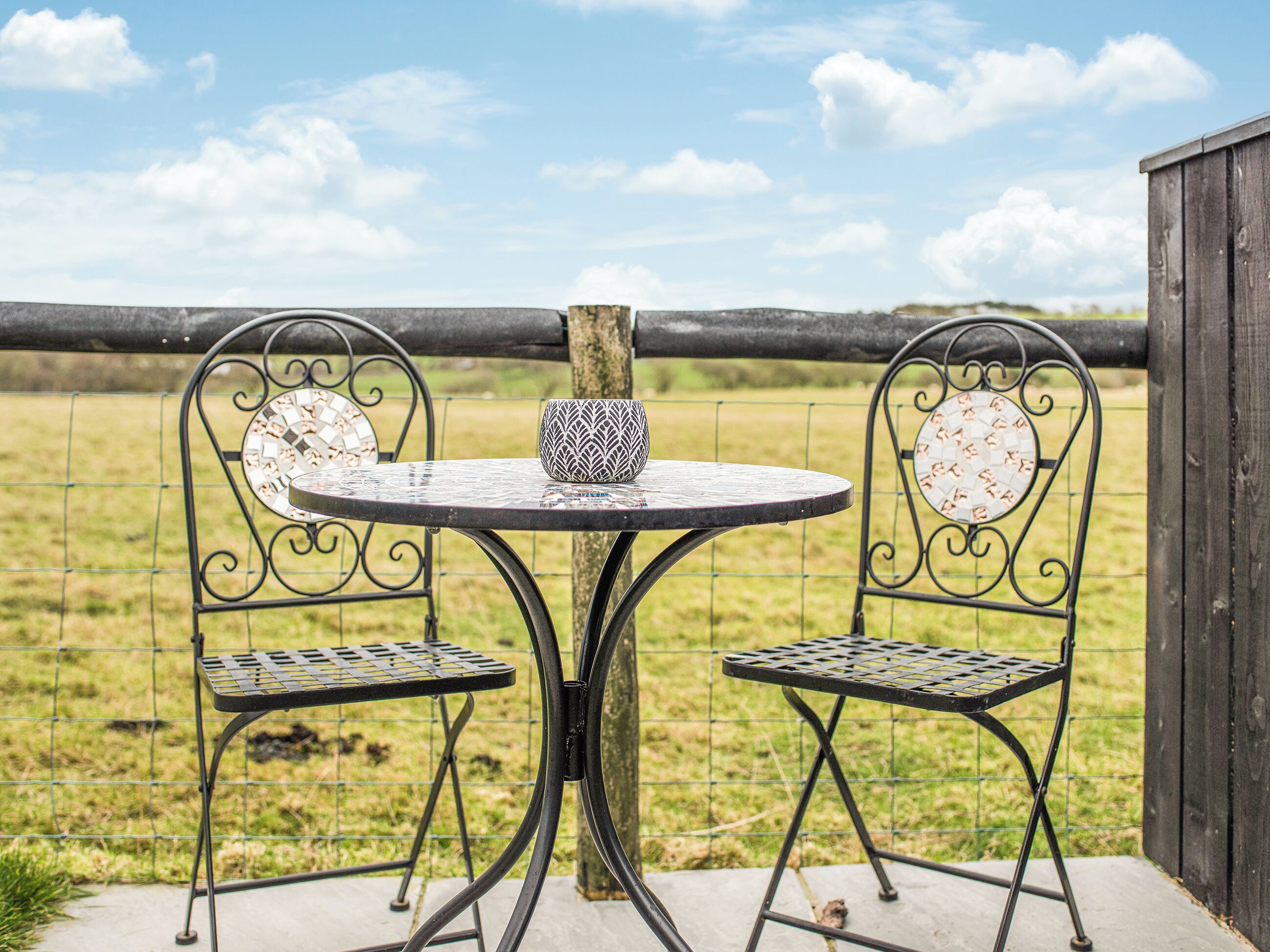 Een set van een metalen tafel en stoelen buiten, met een metalen hek op de achtergrond.