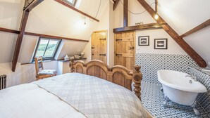 Ein Schlafzimmer mit Bett, Holz-Kopfteil, Fenster, Tür und einem Bad mit Badewanne.