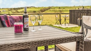 Ein Korbtisch mit einer Flasche, zwei Gläsern, einer Kerze und Blick auf ein grasbewachsenes Feld.