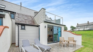 Ein modernes Haus mit einer Holzdiele, zwei Liegestühlen und einem Tisch.