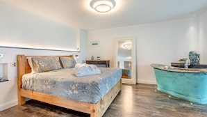 Ein Schlafzimmer mit einem hölzernen Bett, einem Spiegel, einem Badezimmer mit blauer Waschtischkommode und Holzboden.