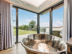 Een moderne badkamer met een groot, glanzend bad, grote ramen en uitzicht op een groen landschap.