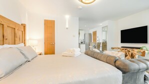 Moderni hotellihuone, jossa on suuri sänky, sohva, televisio ja pieni keittiönurkkaus.