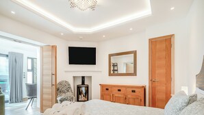 Ein modernes Schlafzimmer mit einem großen Bett, einer Holzkommode, einem Flachbildfernseher und einem Kamin.