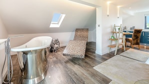 A modern loft bedroom with a skylight, a large bathtub, and a cozy seating area. - Luxurious, 5-star, open plan, first floor apartment designed for two guests. (Bude)