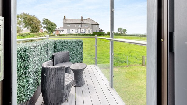 A balcony with wicker furniture and a view of a house and road. - Luxurious, 5-star, open plan, first floor apartment designed for two guests. (Bude)