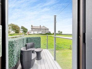 Varanda com móveis de vime e vista para uma casa e estrada.