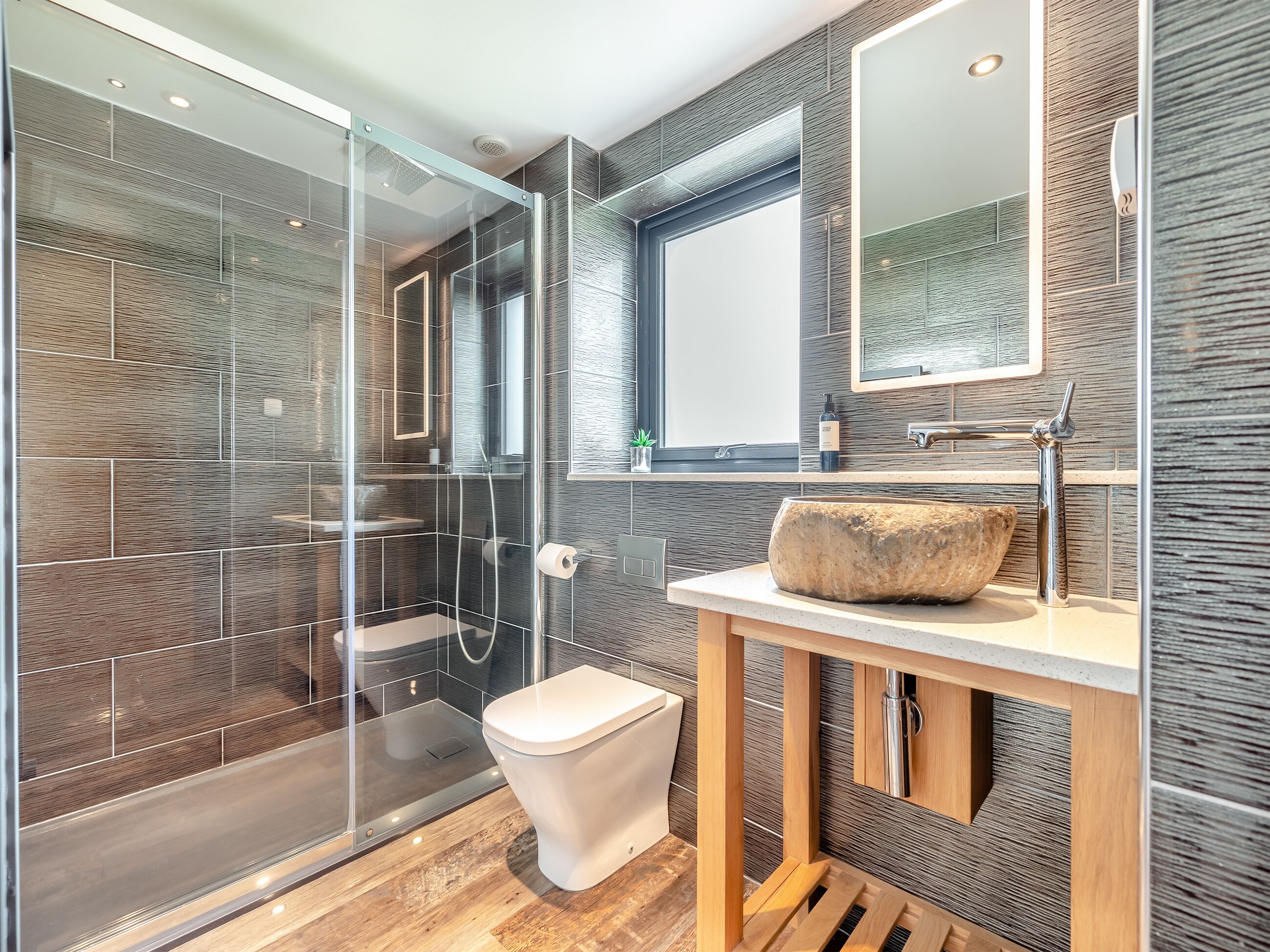 Ein modernes Badezimmer mit Duschkabine aus Glas, Waschtisch aus Holz und einem großen Spiegel.