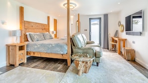 A modern bedroom with a wooden headboard bed, a leather armchair, a glass coffee table, and a TV mounted on the wall. - Luxurious, 5-star, open plan, first floor apartment designed for two guests. (Bude)