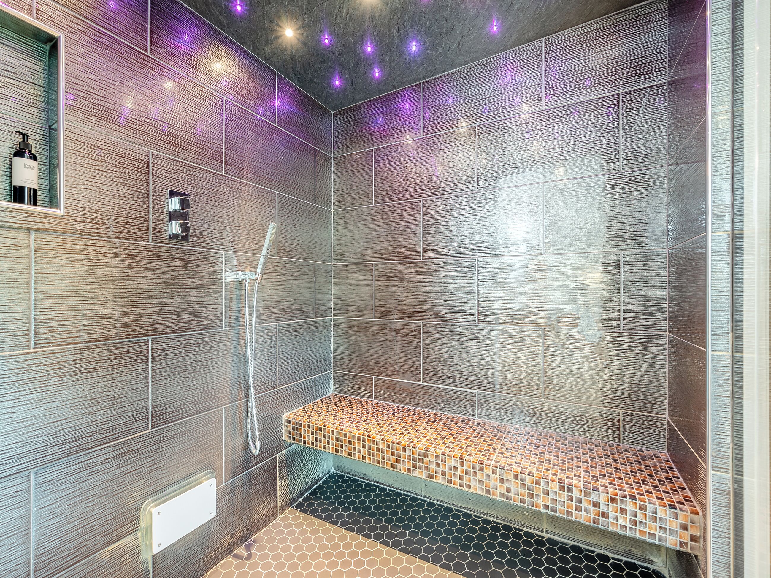 Un baño moderno con pared texturizada, zona de ducha y un banco.