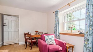 A cozy room with a wooden dining table, chairs, a pink sofa, and a window with floral curtains. - 2 bedroom accommodation in Kildary, near Tain (Kildary, near Tain)