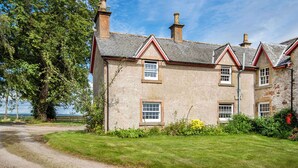 A two-story building with a stone facade, multiple chimneys, and a grassy lawn. - 2 bedroom accommodation in Kildary, near Tain (Kildary, near Tain)