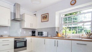 A modern kitchen with white cabinetry, a built-in oven, a microwave, and a window with a view of greenery. - 2 bedroom accommodation in Kildary, near Tain (Kildary, near Tain)