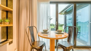 A dining area with a round table, two chairs, a window with a view of a house, and a curtain. - Sun Seeker - UKC6842 (Bude)