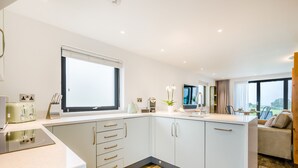 A modern kitchen with a large window, wooden flooring, and a built-in island with a sink. - Sun Seeker - UKC6842 (Bude)