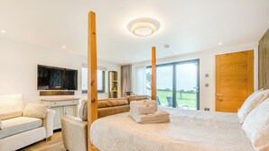 A modern bedroom with a large bed, a sofa, a TV, and a view of the outdoors. - Sun Seeker - UKC6842 (Bude)