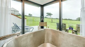 A modern bathroom with a large bathtub, large windows, and a view of a grassy field. - Sun Seeker - UKC6842 (Bude)