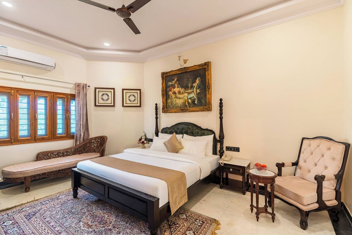 A bedroom with a bed, a chair, a nightstand, a small table, and a painting on the wall.