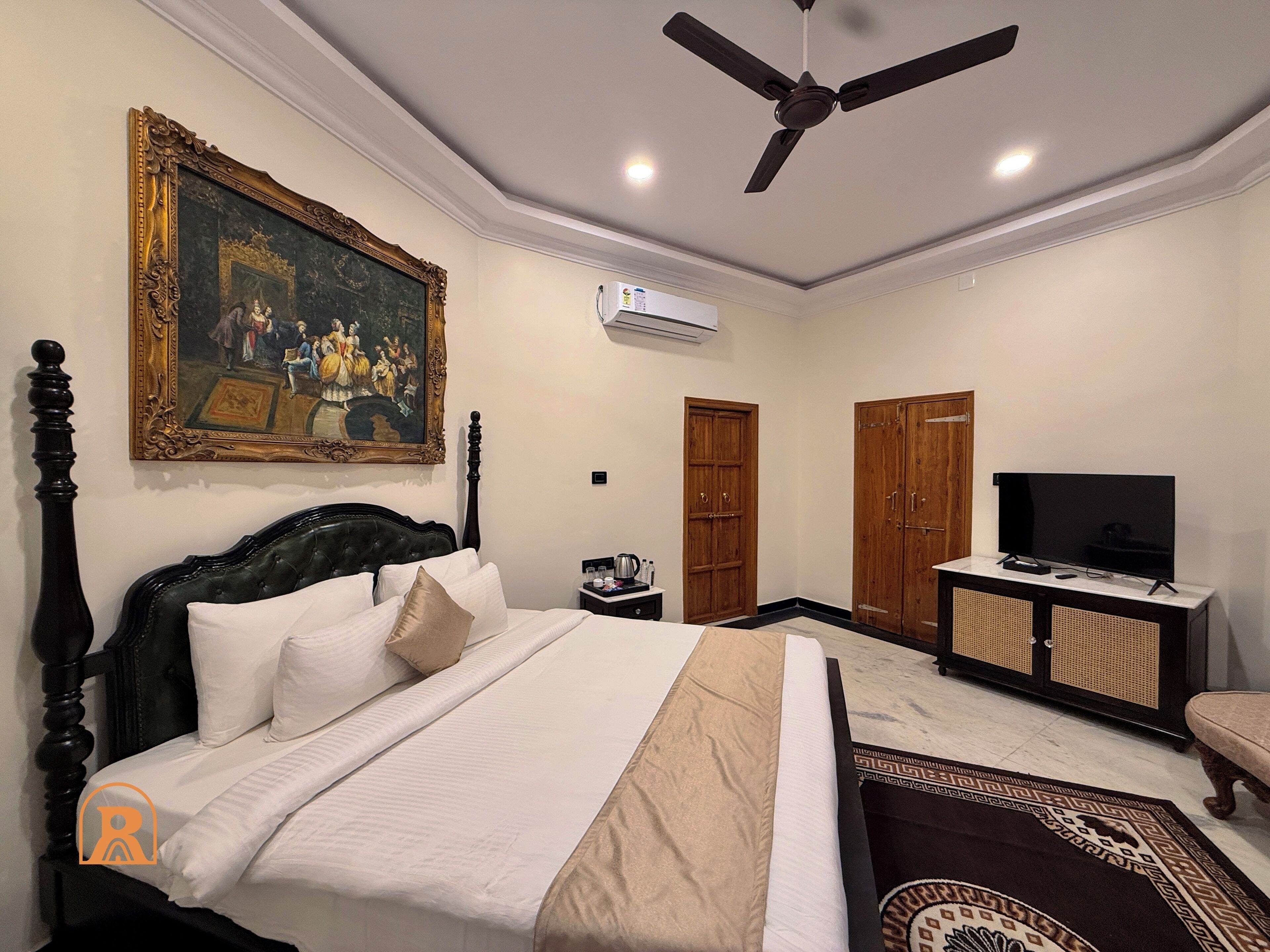 Una habitación de hotel con una cama, ventilador de techo, un cuadro, televisor y armario.
