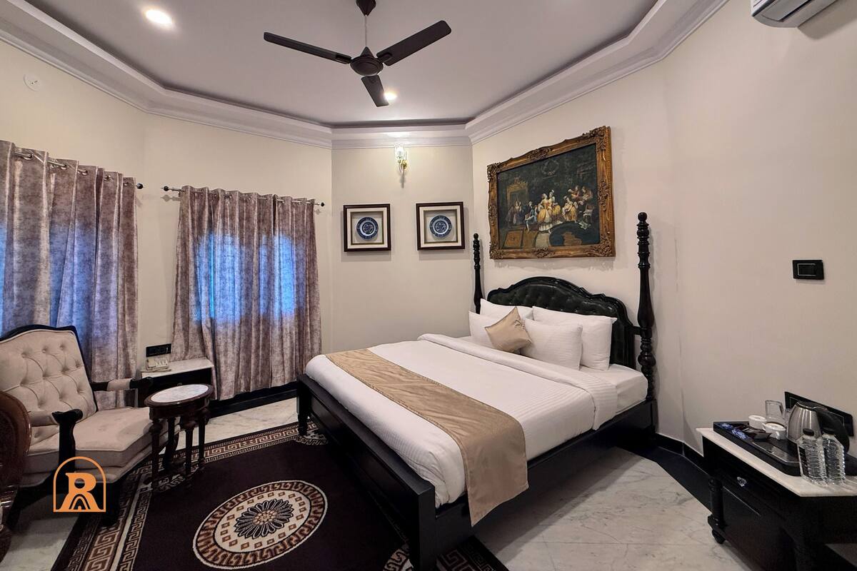 A hotel room with a bed, a chair, a small table, a decorative rug, and a ceiling fan.
