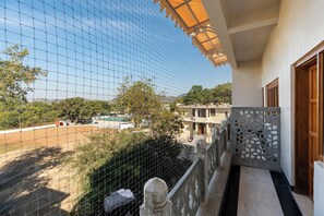 A balcony with a view of a swimming pool and surrounding landscape. - SaffronStays The Shikargarh Palace 8-BR (Udaipur)