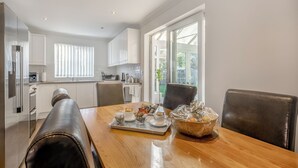 Una cucina moderna con mobili bianchi, un tavolo da pranzo con sedie e vista sull'esterno tramite ampie finestre.