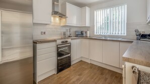 Una cucina moderna con mobili bianchi, forno integrato, microonde e una finestra con persiane verticali.