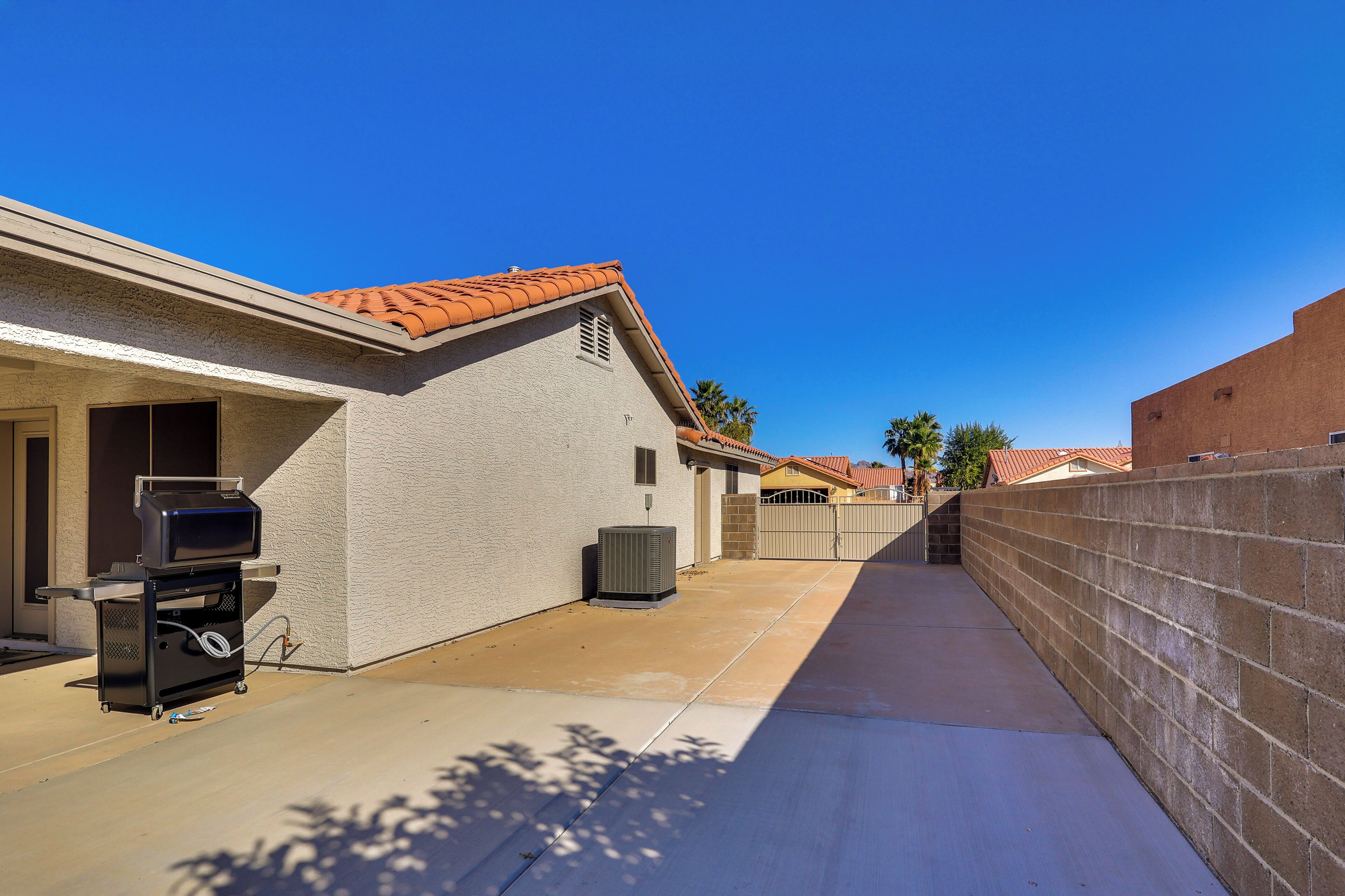 A residential backyard with a barbecue grill, outdoor air conditioning unit, and a concrete patio.