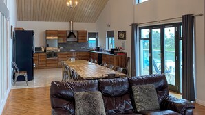 Un'ampia zona giorno con un divano in pelle, un tavolo da pranzo in legno e una cucina sullo sfondo.