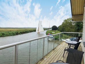 Een terras met uitzicht op een rivier, een zeilboot en een kleine boot die ernaast ligt.