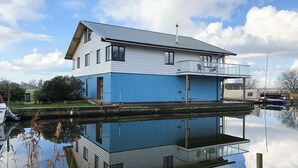 Una casa a due piani con un balcone, affacciata su una superficie d'acqua calma che riflette l'edificio.