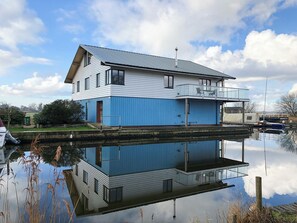 Een herenhuis met balkon, gelegen aan een rustig waterlichaam dat de structuur weerspiegelt.