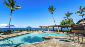 Un espace piscine avec des chaises longues et des parasols, un jacuzzi et une vue sur l’océan.