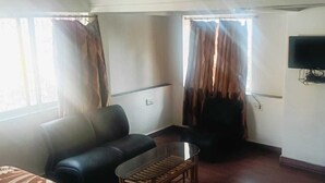 Ett hotellrum med en soffa, ett litet bord, en tv som är monterad på väggen och ett fönster med gardiner.