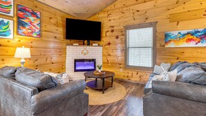 Ein gemütliches Blockhaus-Interieur mit Kamin, zwei Ledersofas, einem Flachbildfernseher und Holzwänden.