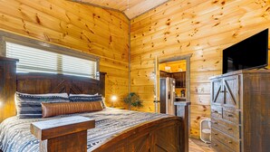 Ein Holzblockhaus-Innenraum mit einem Bett, einem Schminktisch und einem Fernseher.