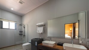 Et moderne badeværelse med en glasbrusekabine, toilet, vask med trækommode og et stort spejl.