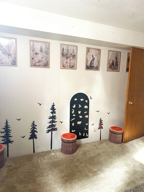 Ein Flur mit einer Wandmalerei zum Thema Wald, gerahmten Bildern und zwei runden Holzhockern.