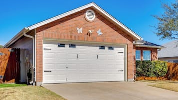 A single-story brick house with a white garage door, a small circular window on the gable, and a butterfly decoration on the wall.
